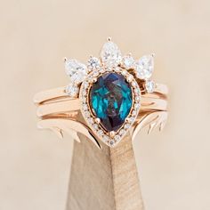 a ring with an oval shaped blue stone surrounded by smaller round diamonds on top of a wooden stand