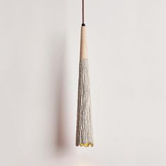 a wooden object hanging from a string on a white wall next to a light bulb