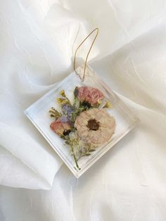 an ornament with dried flowers is hanging on a white fabric background in the shape of a square