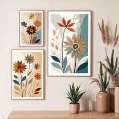 three framed art prints on a wall above a table with potted plants and vases