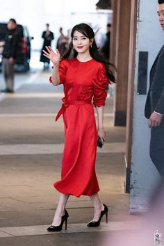 a woman in a red dress is walking down the street with her hand out to someone