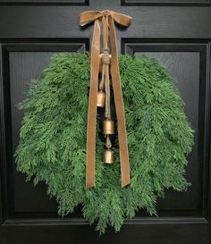 a wreath with two bells hanging from it's side on a black front door