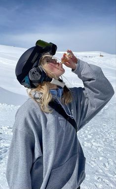 a woman standing on top of a snow covered ski slope drinking from a canister