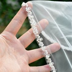 a hand holding a white veil with flowers on the side and pearls attached to it