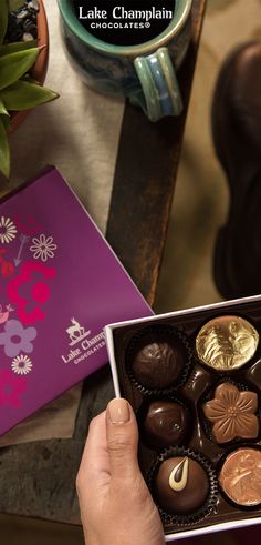 a person holding a box of chocolates in front of a table with other items