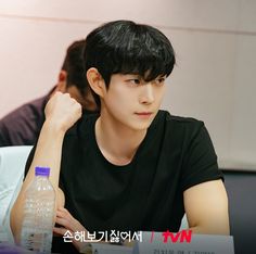 a young man sitting at a table with a bottle of water in front of him