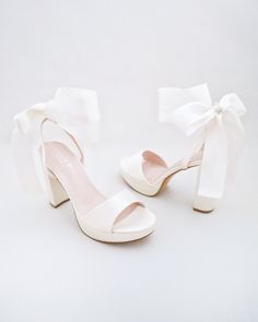 a pair of white high heeled shoes with a bow