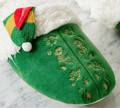 a green slipper with a red and yellow hat on it's head sitting on a marble surface