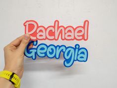 someone is holding up the word rachael in front of a white wall with blue and red lettering