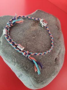 a bracelet with skulls and tassels on top of a rock in front of a red background