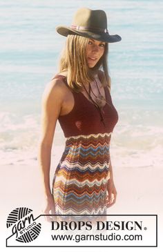 a woman standing on top of a sandy beach next to the ocean wearing a hat