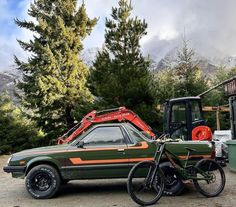 a green car with an orange stripe parked next to a red and black bike in front of some trees