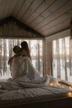 two people sitting on top of a bed in a room filled with snow covered trees