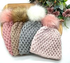 four knitted hats with pom - poms sitting on top of each other