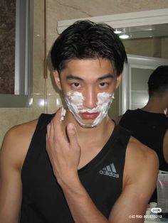 a young man shaving his face in the bathroom with white paper on his face