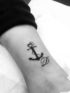 a black and white photo of a small anchor tattoo on the ankle, which reads love