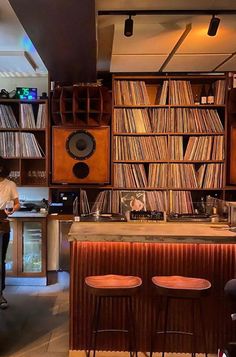 a man standing in front of a bar with lots of records on the walls and shelves