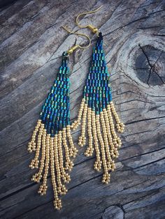 the beaded fringe earrings are hanging from gold hooks on a wooden table with wood planks