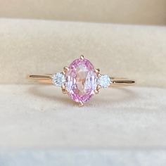 a pink and white diamond ring sitting on top of a cushioned surface in a box