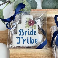 a bride tribe cookie in a clear box with blue ribbon and flowers on the side