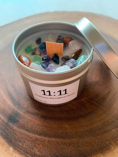 a cup filled with lots of different colored rocks on top of a wooden table next to a metal spoon