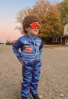 a young boy in a blue space suit and red goggles standing on the street