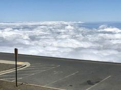 an empty parking lot in the middle of some clouds with a street sign next to it