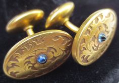 Now here's one sharp looking pair of antique cufflinks! Ready to dress up your finest attire. These beauties date from the late 1800's time period. Made of 14K yellow gold. The pair is hallmarked and has been tested to ensure the golds purity. Wonderful foliage and floral motifs adorn the main panel. In its center is a lovely tiny sapphire cabochon stone. The ovals measure 11/16 of an inch by 7/16 of an inch. The center bar is approximately 3/8 of an inch long. Ends are engraved with the letters Victorian Engraved Earrings For Formal Occasions, Victorian Formal Jewelry With Screw Back, Victorian Screw Back Jewelry For Formal Occasions, Victorian Screw Back Earrings For Formal Occasions, Antique Screw Back Earrings For Formal Occasions, Antique Formal Earrings Stamped 14k, Antique Stamped 14k Formal Earrings, Formal Oval Jewelry With Maker's Mark, Vintage Yellow Gold Cufflinks For Wedding