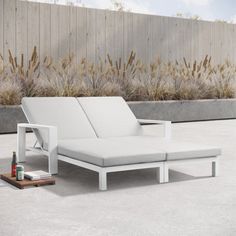 a white chaise lounger sitting on top of a cement floor next to a wooden fence