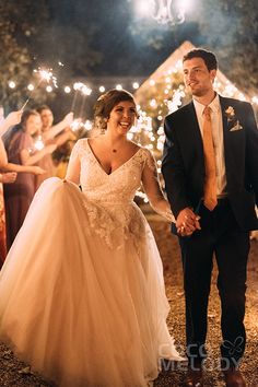 a bride and groom holding hands as they walk down the aisle with sparklers in the background