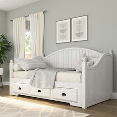 a white daybed with drawers underneath it in a room next to a potted plant