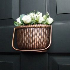 a brown basket with white flowers hanging from it's side on a black door