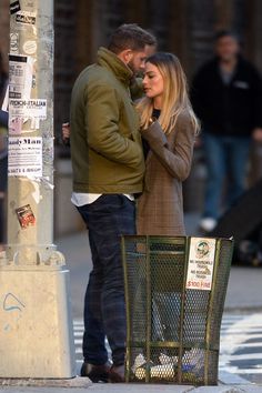 a man and woman standing next to each other near a pole on a city street