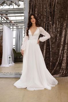 a woman standing in front of a mirror wearing a white wedding dress with long sleeves