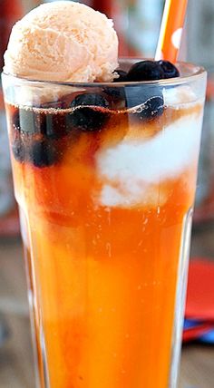 a tall glass filled with ice cream and blueberries on top of a wooden table