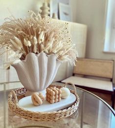 a glass table topped with a white vase filled with flowers and seashells on top of it