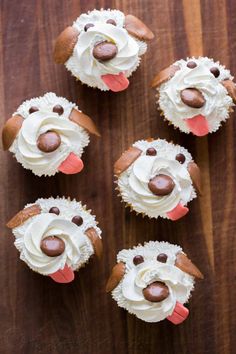 four cupcakes with frosting and dog faces on them sitting on a wooden table