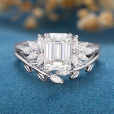 an emerald cut diamond ring with leaves on the band and side stones set in 18k white gold