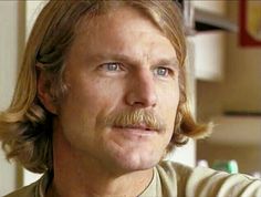 a man with long hair and a moustache on his face looking at the camera