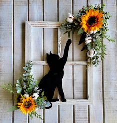 a black cat sitting on top of a wooden frame with flowers and greenery around it