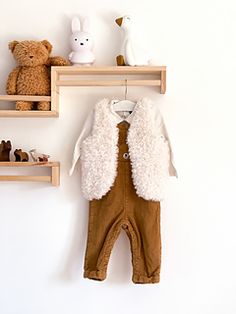 a baby's outfit hanging on the wall next to shelves with teddy bears and other toys