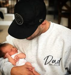 a man holding a baby in his arms while wearing a dad hat and looking at the camera