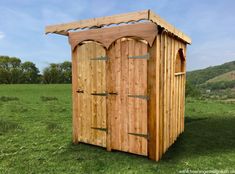 a small wooden outhouse sitting on top of a lush green field