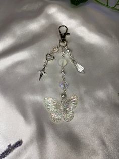 a keychain with a butterfly and charms attached to it's side on a silver satin surface