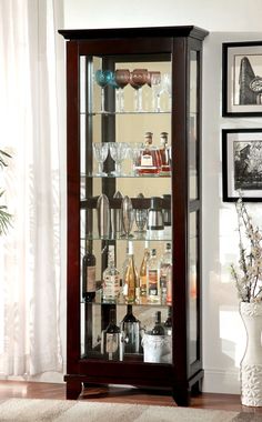 a display case with wine glasses and liquor bottles on it's glass shelves in a living room