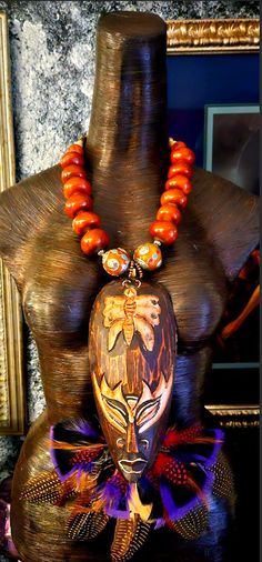 A wild and exotic tribal or ethnic chest piece - statement pendant is yours if you are brave enough to rock such a piece! A earth tone carved wood mask from Bali with a butterfly motif hosts feathers among the bottom portion adding texture and color. An oversized orange-brown Moroccan resin beaded necklace suspends the mask portion. The necklace adjusts from 23-26" and closes with gold tone hardware and a lobster claw clasp. Two ornate Tibetan beads with inlaid turquoise and coral flank the pendant. The pendant measures approximately 13" x 10". This is a surpringly lightweight piece considering all of the components. The back of the necklace is a mix of round coral, wood and gold tone tribal metal spacers. A MUST HAVE for your Autumn wardrobe! From the Atelier of Kat Kouture. Bohemian Hand Painted Necklaces For Festivals, Bohemian Hand Painted Festival Necklaces, Bohemian Brown Hand Painted Necklaces, Bohemian Hand Painted Brown Necklace, Bohemian Brown Hand Painted Necklace, Traditional Hand Painted Necklaces For Festivals, Traditional Hand Painted Festival Necklaces, Mask With Feathers, Rocker Chic Accessories