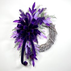 a wreath with purple flowers and greenery hanging from it's side on a white surface