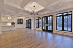 an empty living room with wood floors and large windows in the center is lit by recessed lights