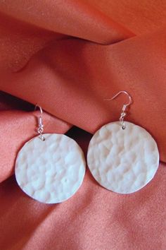 two white circles are hanging from silver earwires on an orange fabric background,