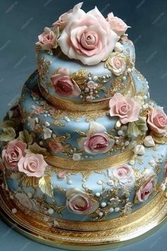 a three tiered blue cake with pink roses on the top and gold trimmings